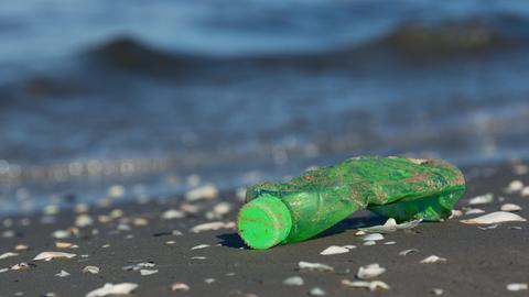 Nahaufnahme einer angespülten grünen Plastikflasch an einem Strand.