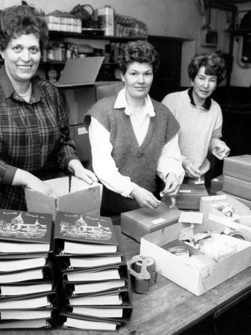 Das Schwarz-Weiß-Foto zeigt drei der Geseker Landfrauen mit mehreren Stapeln von Päckchen und Rezeptbüchern vor sich.