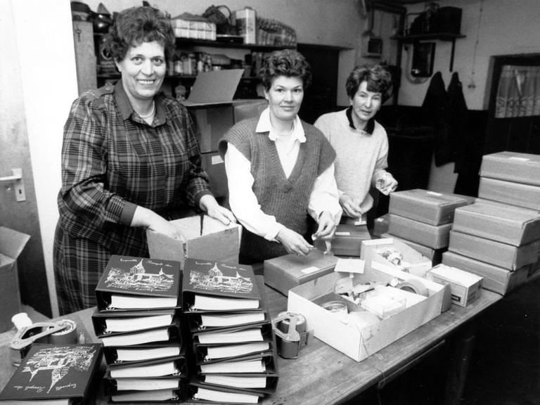 Das Schwarz-Weiß-Foto zeigt drei der Geseker Landfrauen mit mehreren Stapeln von Päckchen und Rezeptbüchern vor sich.