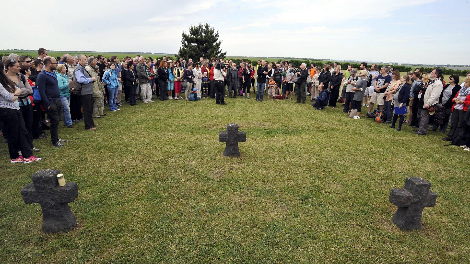 Eine große Menschenansammlung steht auf einer Wiese um drei steinerne Gedenkkreuze herum. Eine große Menschenansammlung steht auf einer Wiese um drei steinerne Gedenkkreuze herum.