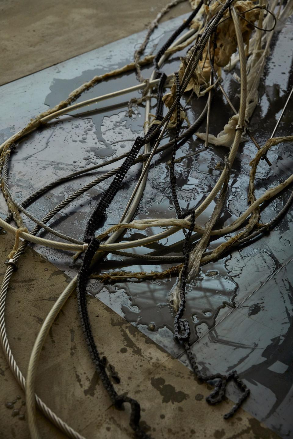 Blick in die Ausstellung: Schmutzige Seilen und Ketten auf dem Boden.