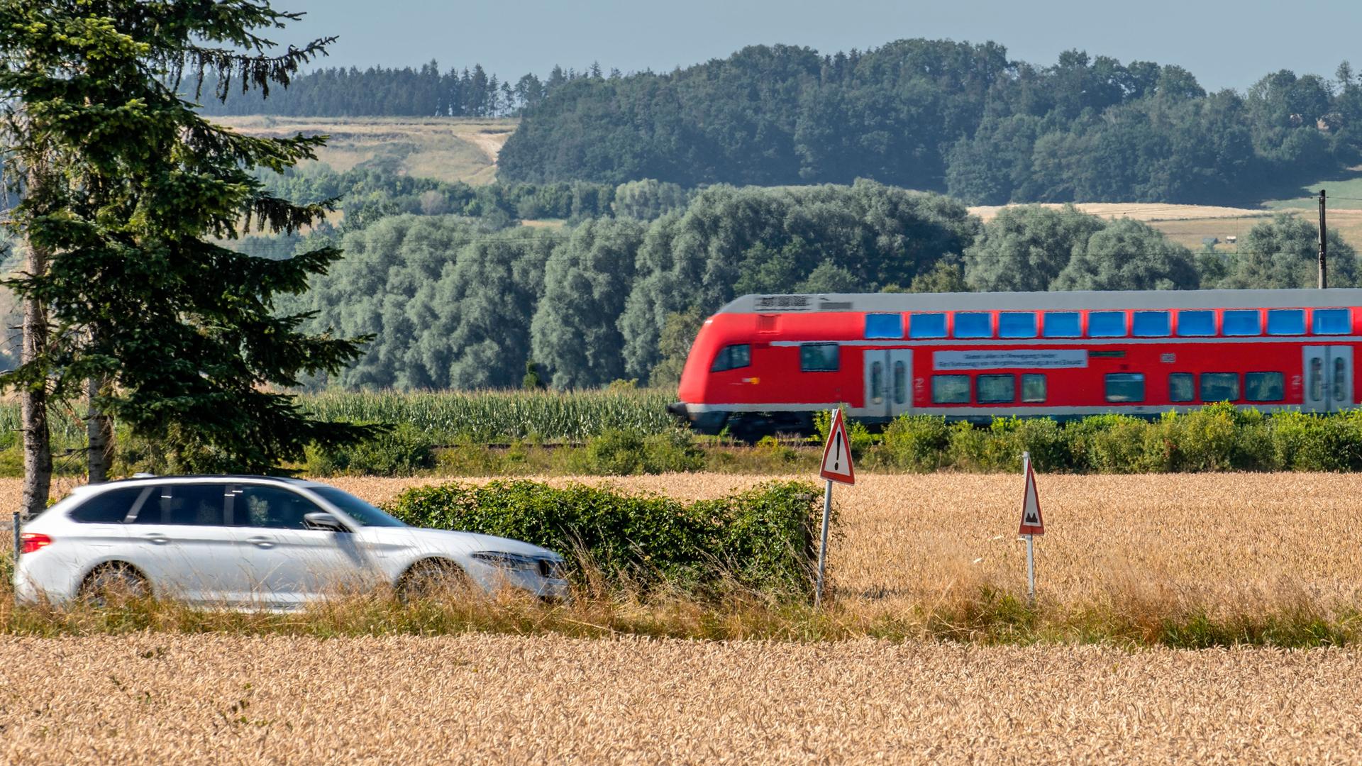 Ein Auto und ein Regionalzug fahren durch eine Landschaft mit Wäldern und Feldern. Ein Auto und ein Regionalzug fahren durch eine Landschaft mit Wäldern und Feldern.