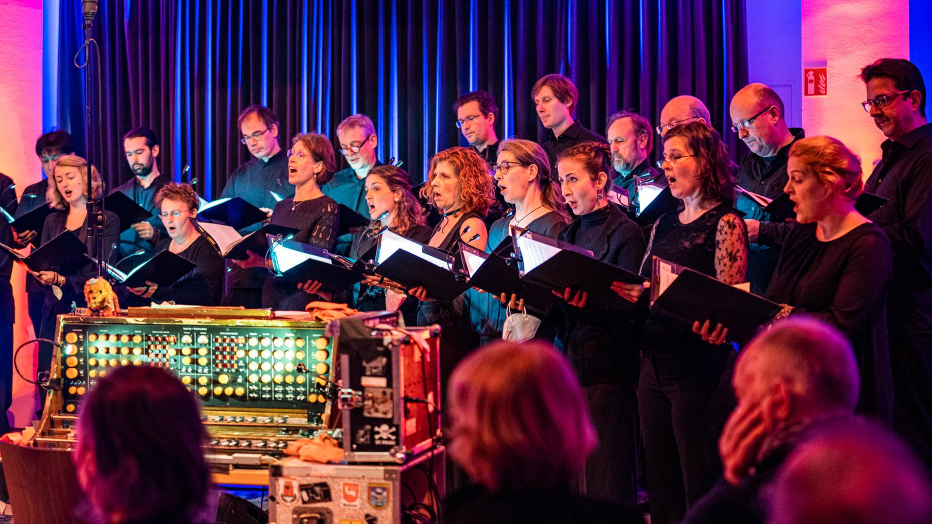 Die Sängerinnen und Sänger des Rundfunkchores Berlin stehen versammelt um ein Trautorium und singen. Die Sängerinnen und Sänger des Rundfunkchores Berlin stehen versammelt um ein Trautorium und singen.