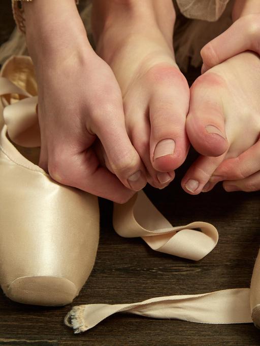 Eine Balletttänzerin zieht nach dem Training ihre Spitzenschuhe aus und knetet ihre Zehen.