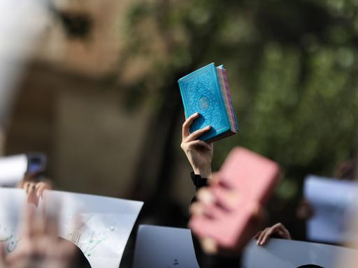 Eine hand hält bei einer Demonstration den blau eingebundenen Koran in die Höhe.