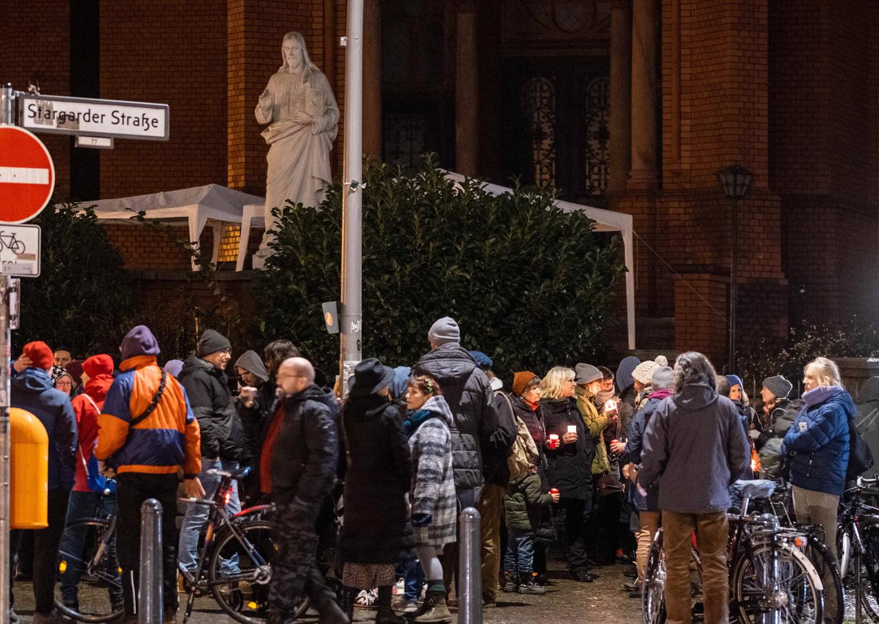 Eine Menschengruppe, teilweisen mit brennenden Kerzen in den Händen, steht in der Nacht vor einer Backsteinkirche. Eine Menschengruppe, teilweisen mit brennenden Kerzen in den Händen, steht in der Nacht vor einer Backsteinkirche.
