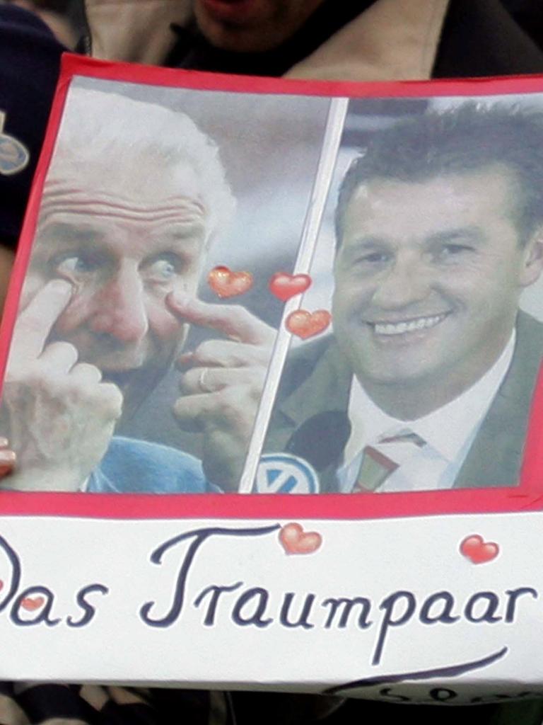 Fans halten ein Plakat mit den Bildern von Giovanni Trapattoni und Thomas Strunz hoch. Darunter steht: "Das Traumpaar der Liga?" und "Wird diesmal alles besser?". 