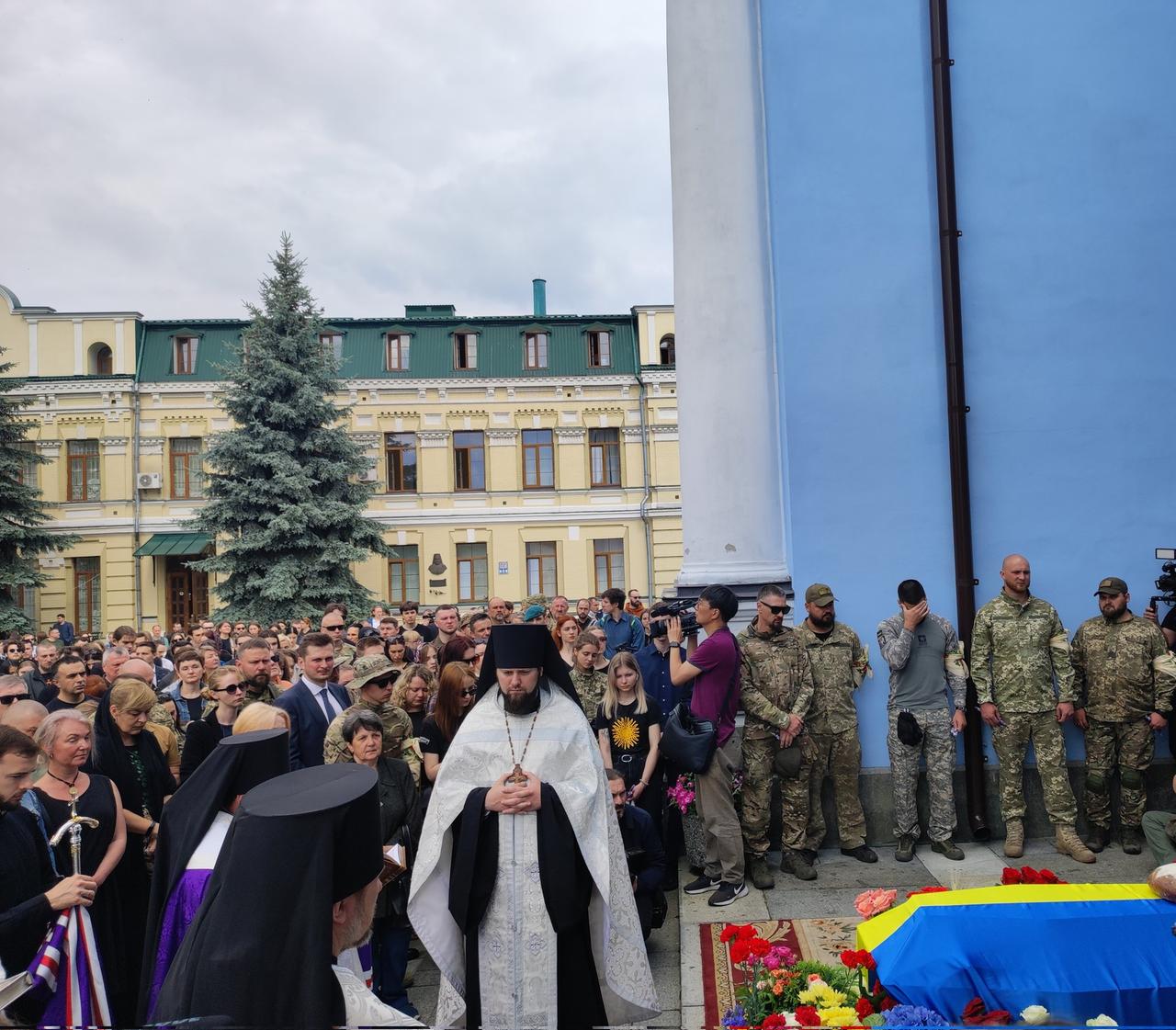 Gedenkgottesdienst auf einem Platz in Kiew. Neben einem Sarg, der mit der ukrainischen Flagge bedeckt, stehen etliche trauernde Menschen. Gedenkgottesdienst auf einem Platz in Kiew. Neben einem Sarg, der mit der ukrainischen Flagge bedeckt, stehen etliche trauernde Menschen.