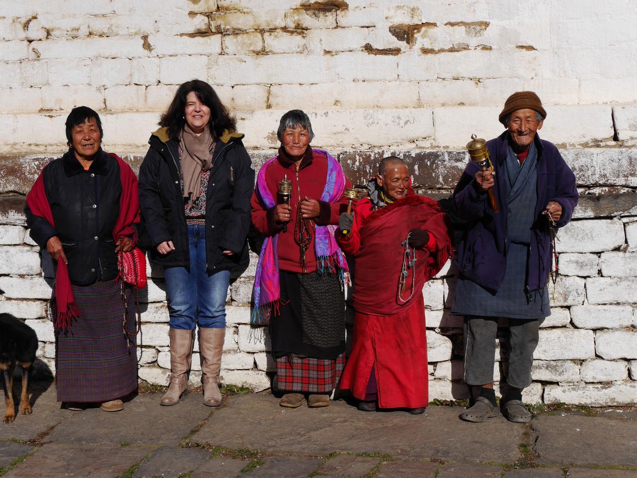 Eine Gruppe lächelnder Bhutanerinnen und Bhutanern in traditioneller Kleidung mit der Reiseagentin Bernita Müller. Eine Gruppe lächelnder Bhutanerinnen und Bhutanern in traditioneller Kleidung mit der Reiseagentin Bernita Müller.