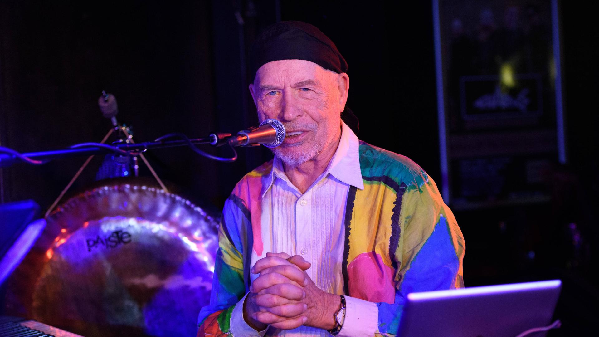 Der Musiker Don Preston während eines Konzerts auf der Bühne des Berliner Clubs Quadimodo. Er trägt eine kurze, dunkle Wollmütze und singt mit gefalteten Händen in ein Mikrofon. Der Musiker Don Preston während eines Konzerts auf der Bühne des Berliner Clubs Quadimodo. Er trägt eine kurze, dunkle Wollmütze und singt mit gefalteten Händen in ein Mikrofon.