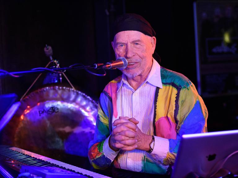 Der Musiker Don Preston während eines Konzerts auf der Bühne des Berliner Clubs Quadimodo. Er trägt eine kurze, dunkle Wollmütze und singt mit gefalteten Händen in ein Mikrofon.