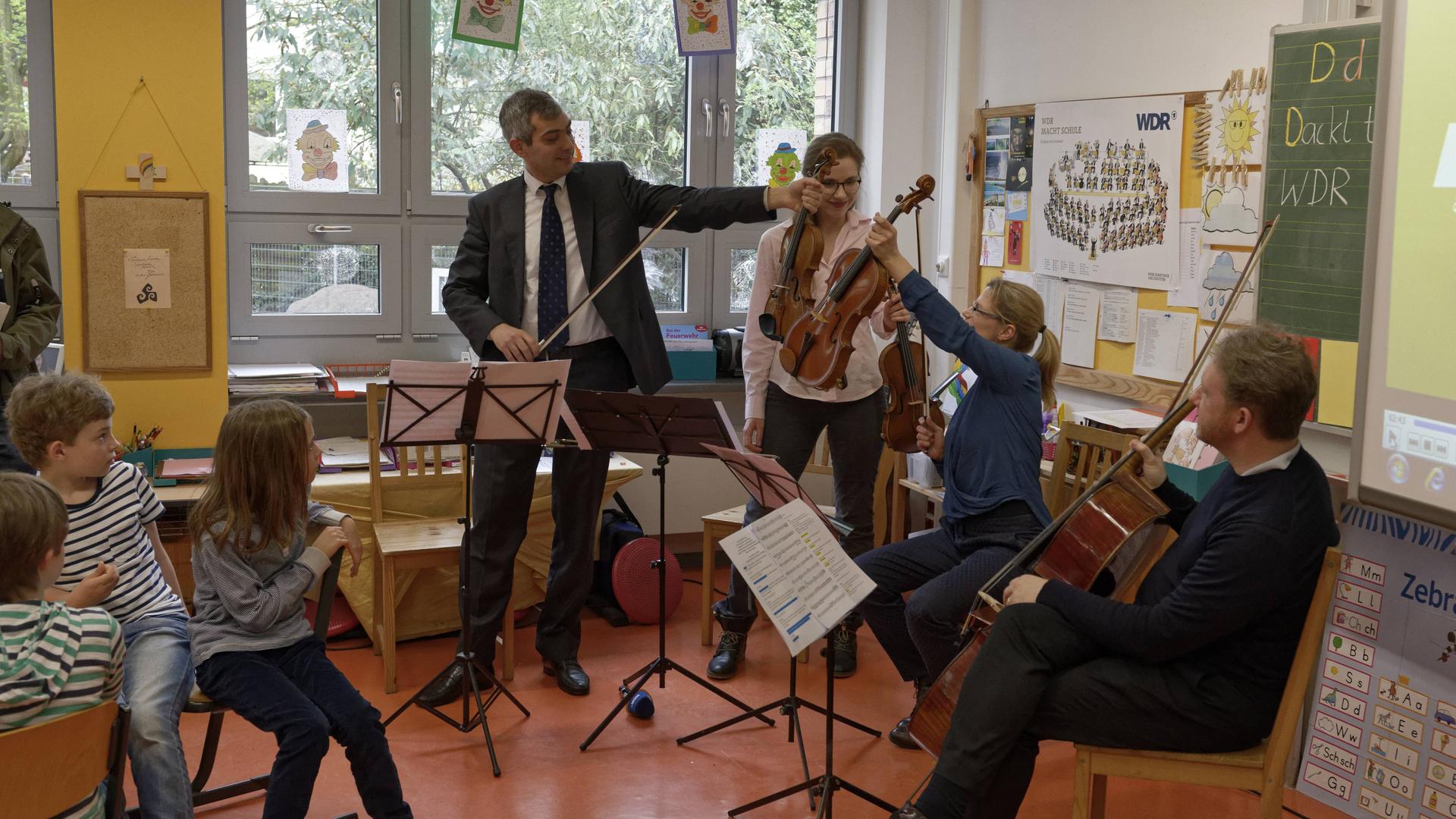 Ein Streicherquartett des WDR Sinfonieorchesters sitzt mit Instrumenten in einer Klasse bei einem Schulbesuch. Ein Streicherquartett des WDR Sinfonieorchesters sitzt mit Instrumenten in einer Klasse bei einem Schulbesuch.