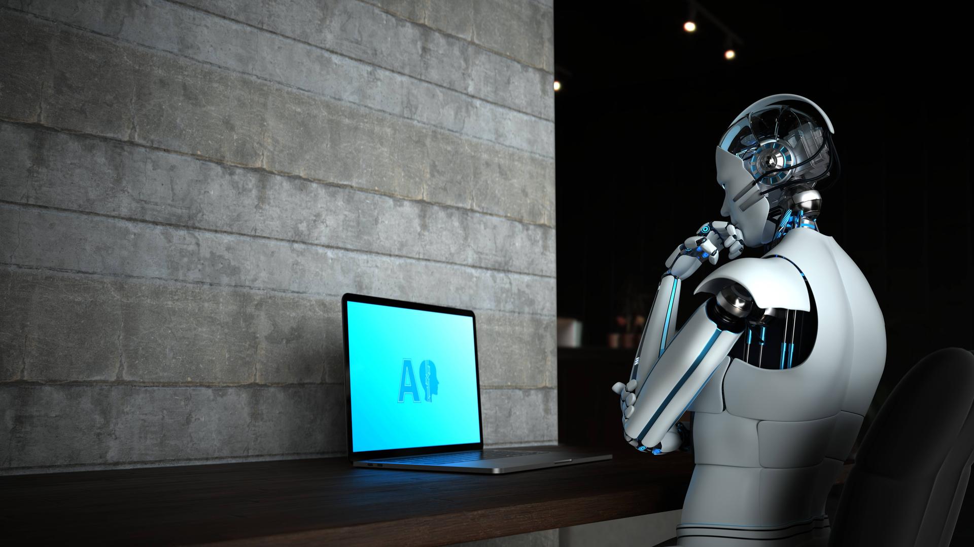 Ein Roboter mit menschlicher Erscheinung blickt auf einen Laptop auf dem die Buchstaben AI zu sehen sind.