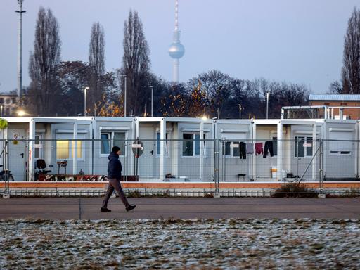 Umzäunte Flüchtlingsunterkunft aus Containern auf dem Tempelhofer Feld, im Hintergrund der Fernsehturm von Berlin.