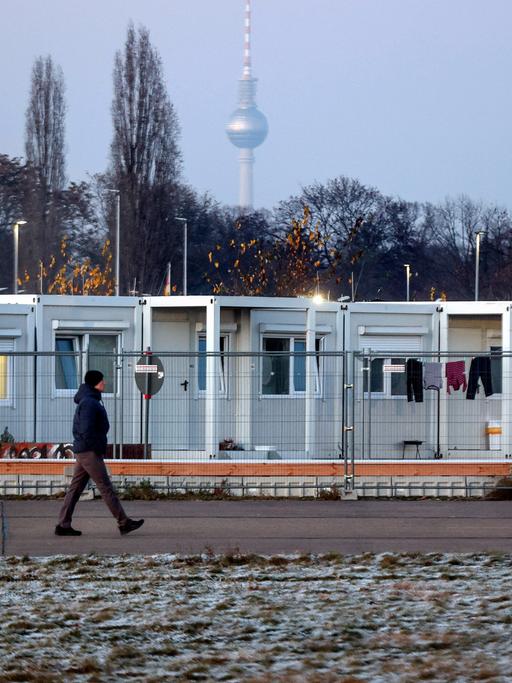 Umzäunte Flüchtlingsunterkunft aus Containern auf dem Tempelhofer Feld, im Hintergrund der Fernsehturm von Berlin.