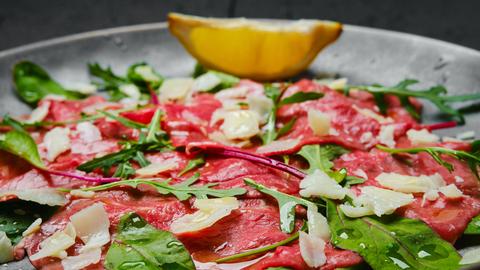 Marmoriertes Rindercarpaccio mit Rucola- und Mangoldblättern, Zitrone und Parmesankäse auf dunklem Hintergrund