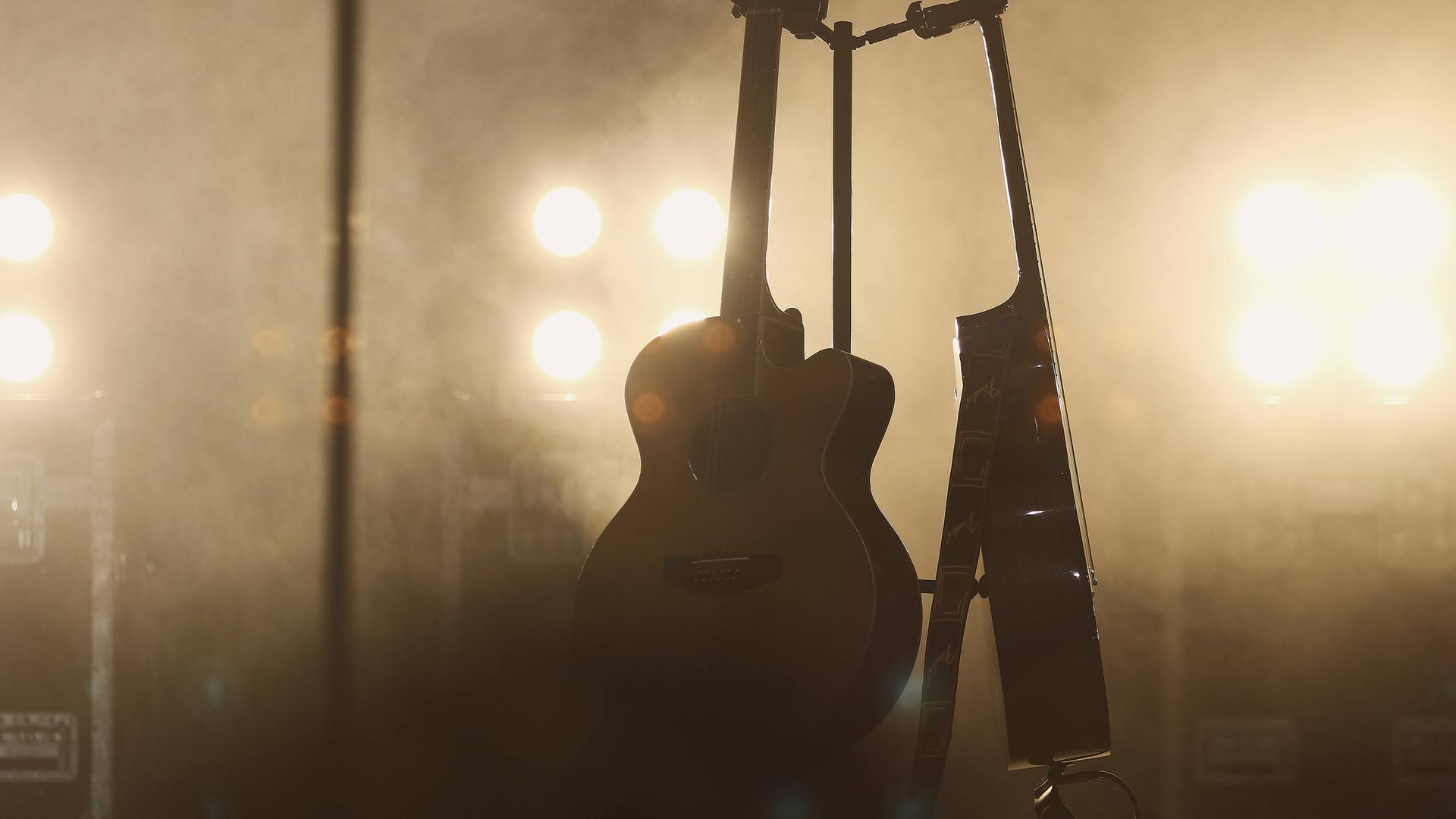 Zwei Gitarren stehen im Bühnennebel. Von hinten leuchten Scheinwerfer. Zwei Gitarren stehen im Bühnennebel. Von hinten leuchten Scheinwerfer.