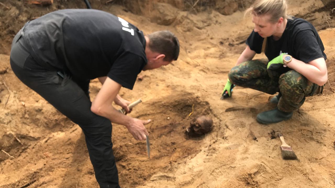 Ein Mann und eine Frau arbeiten in einer ausgehobenen Grube. Unter anderem liegt ein Pinsel in der Grube bei einem gefundenen Schädel.