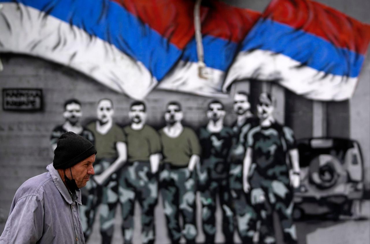 A man walks by graffiti that showing Serbian flags and soldiers in northern, Serb-dominated part of ethnically divided town of Mitrovica, Kosovo, Friday, Oct. 15, 2021. Tensions between Kosovo and Serbia resumed Wednesday after Kosovo police clashed with ethnic Serbs during an anti-smuggling operation. Kosovo, a Serbian province before it declared independence in 2008, was in a war in 1998-1999 between Serbian troops and ethnic Albanian separatists fighting for independence until a NATO air campaign pushed Serb forces away. (AP Photo/Darko Vojinovic) A man walks by graffiti that showing Serbian flags and soldiers in northern, Serb-dominated part of ethnically divided town of Mitrovica, Kosovo, Friday, Oct. 15, 2021. Tensions between Kosovo and Serbia resumed Wednesday after Kosovo police clashed with ethnic Serbs during an anti-smuggling operation. Kosovo, a Serbian province before it declared independence in 2008, was in a war in 1998-1999 between Serbian troops and ethnic Albanian separatists fighting for independence until a NATO air campaign pushed Serb forces away. (AP Photo/Darko Vojinovic)