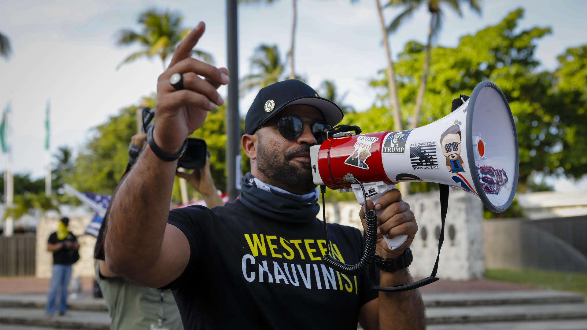 Ein Mann mit einem T-Shirt mit der Aufschrift "Western Chauvinist" spricht in ein mit Trump-Stickern beklebtes Megafon. Ein Mann mit einem T-Shirt mit der Aufschrift "Western Chauvinist" spricht in ein mit Trump-Stickern beklebtes Megafon.