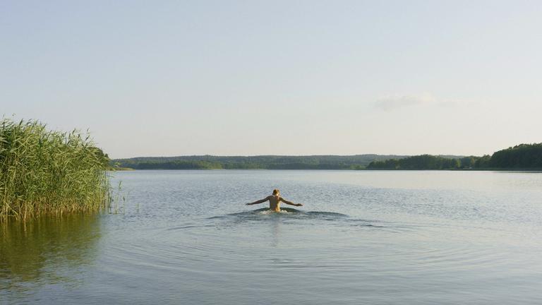 Ein Junge schwimmt alleine in einem sonnigen, ruhigen See in der Uckermark.
