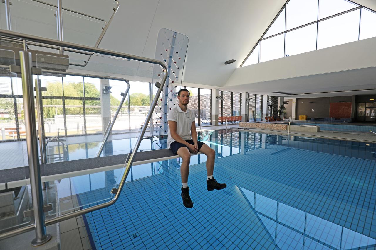Ein Bademeister sitzt im leeren Hallenbad auf einem Sprungbrett. Ein Bademeister sitzt im leeren Hallenbad auf einem Sprungbrett.