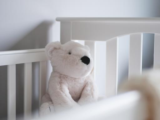 Ein weißer Teddybär sitzt ein einem weißen Kinderbett.