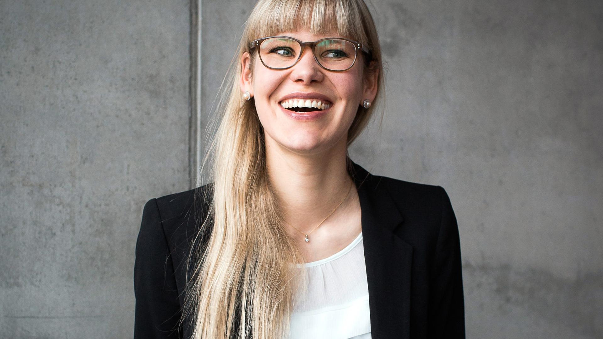 Die Psychologie-Professorin Eva Asselmann steht vor einer grauen Betonwand und guckt lachend zur Seite aus dem Bild hinaus. Die Psychologie-Professorin Eva Asselmann steht vor einer grauen Betonwand und guckt lachend zur Seite aus dem Bild hinaus.