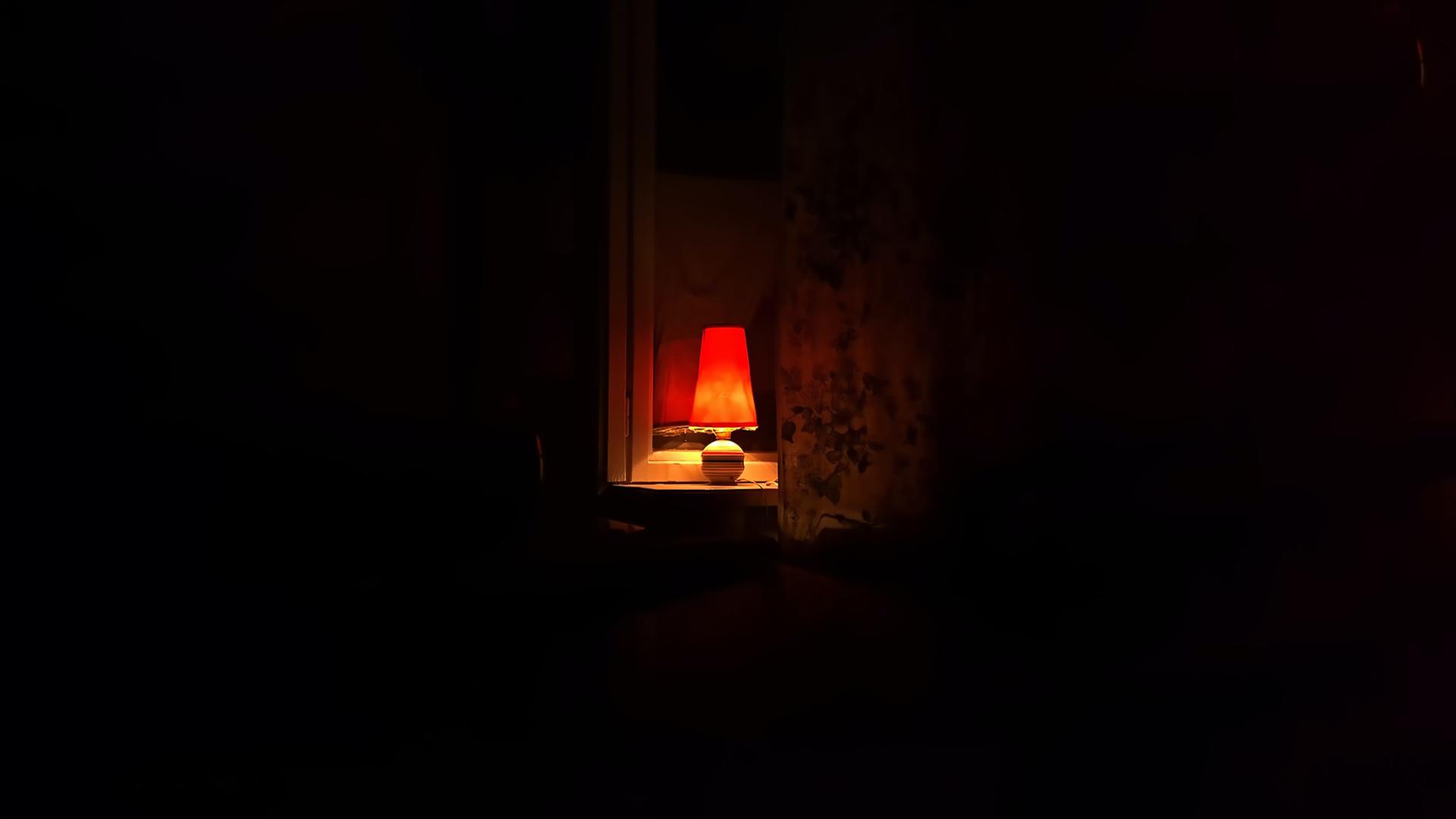 Eine kleine Lampe leuchtet in einem Zimmer in die Dunkelheit.