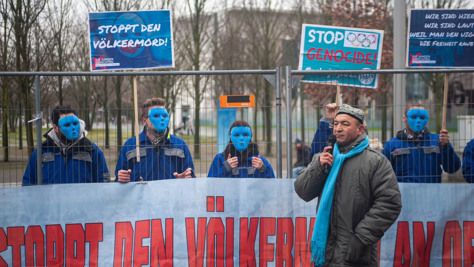 Asgar Can, Vorsitzender der Ostturkistanischen Union Uigurische Gemeinde bei einer Rede waehrend einer Kundgebung vor dem Bundeskanzleramt im Bezirk Berlin-Mitte. Dahinter protestieren maskierte Demonstranten der Aktivistengruppe Die Jungen Gerechten mit Transparenten und Protestplakaten gegen den Voelkermord an den Uiguren in der chinesischen autonomen Region Xinjiang und der Einhaltung der Menschenrechte und fordern einen diplomatischen Boykott der Olympischen Winterspiele 2022 in Peking. Asgar Can, Vorsitzender der Ostturkistanischen Union Uigurische Gemeinde bei einer Rede waehrend einer Kundgebung vor dem Bundeskanzleramt im Bezirk Berlin-Mitte. Dahinter protestieren maskierte Demonstranten der Aktivistengruppe Die Jungen Gerechten mit Transparenten und Protestplakaten gegen den Voelkermord an den Uiguren in der chinesischen autonomen Region Xinjiang und der Einhaltung der Menschenrechte und fordern einen diplomatischen Boykott der Olympischen Winterspiele 2022 in Peking.