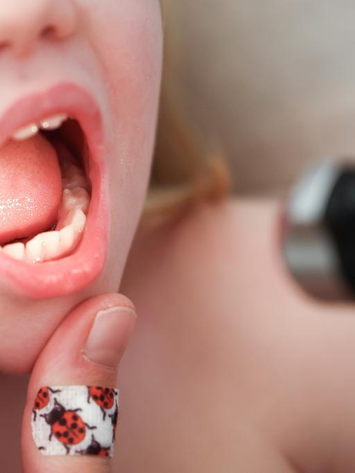 Mit einem Otoskop untersucht eine Kinderärztin den Mund und Hals eines Mädchens.