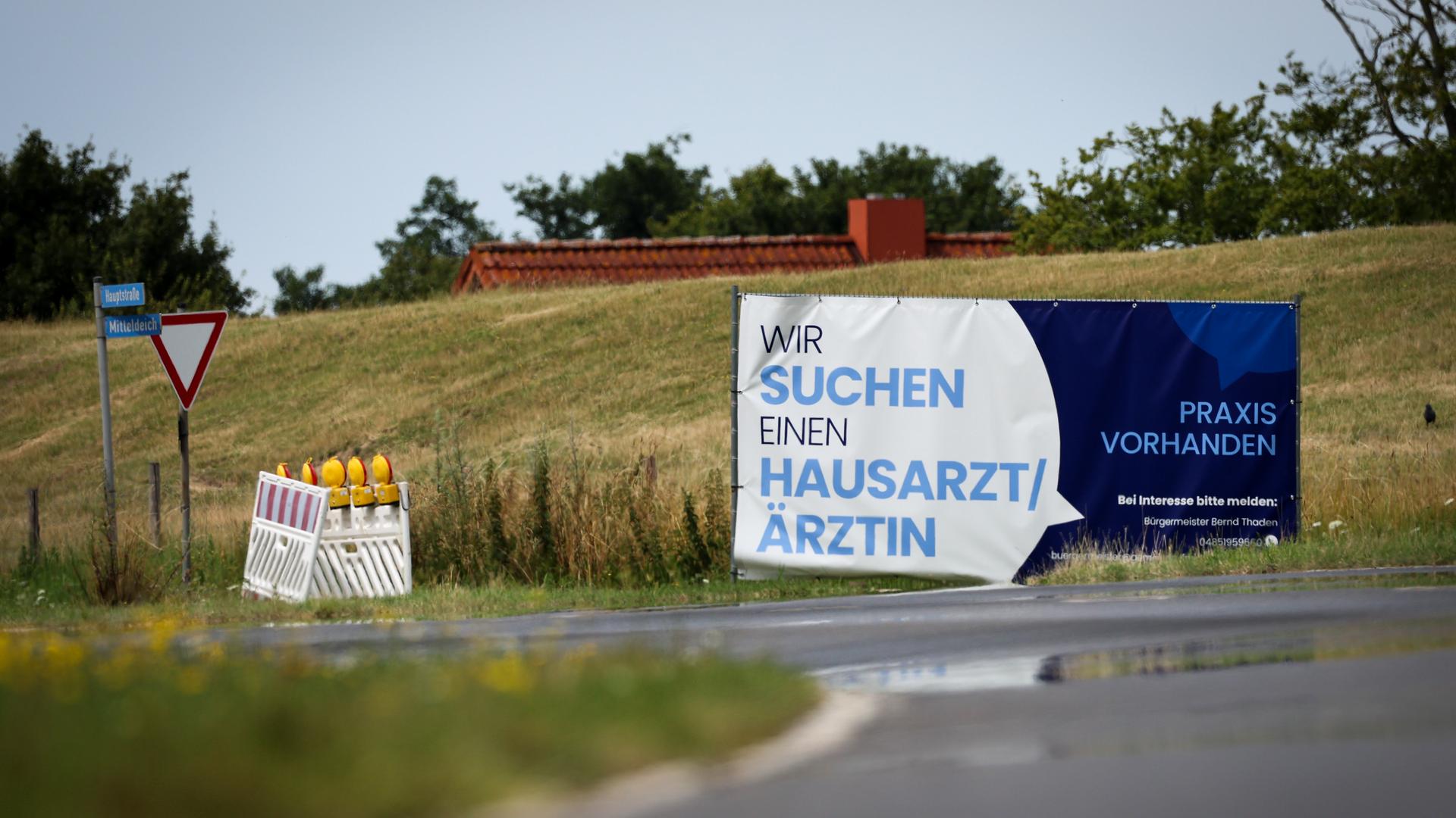 Ein Plakat mit dem Text "Wir suchen einen Hausarzt / Ãrztin - Praxis Vorhanden" steht am Ortseingang von Friederichskoog. Hausärzte werden in vielen ländlichen Regionen gesucht. Ein Plakat mit dem Text "Wir suchen einen Hausarzt / Ãrztin - Praxis Vorhanden" steht am Ortseingang von Friederichskoog. Hausärzte werden in vielen ländlichen Regionen gesucht.