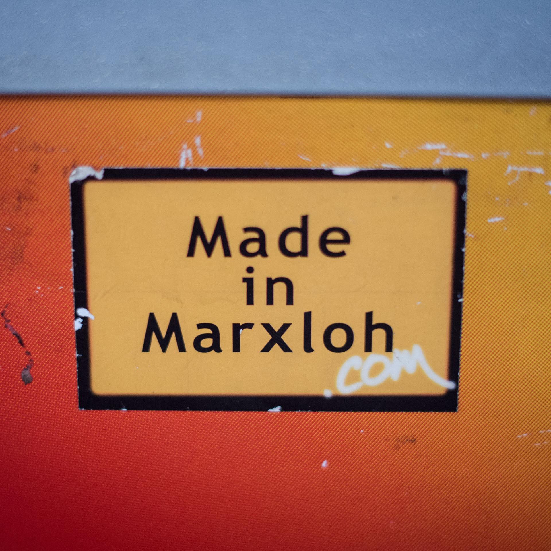 Ein Aufkleber "Made in Marxloh" klebt an einer orangfarbenen Wand.
