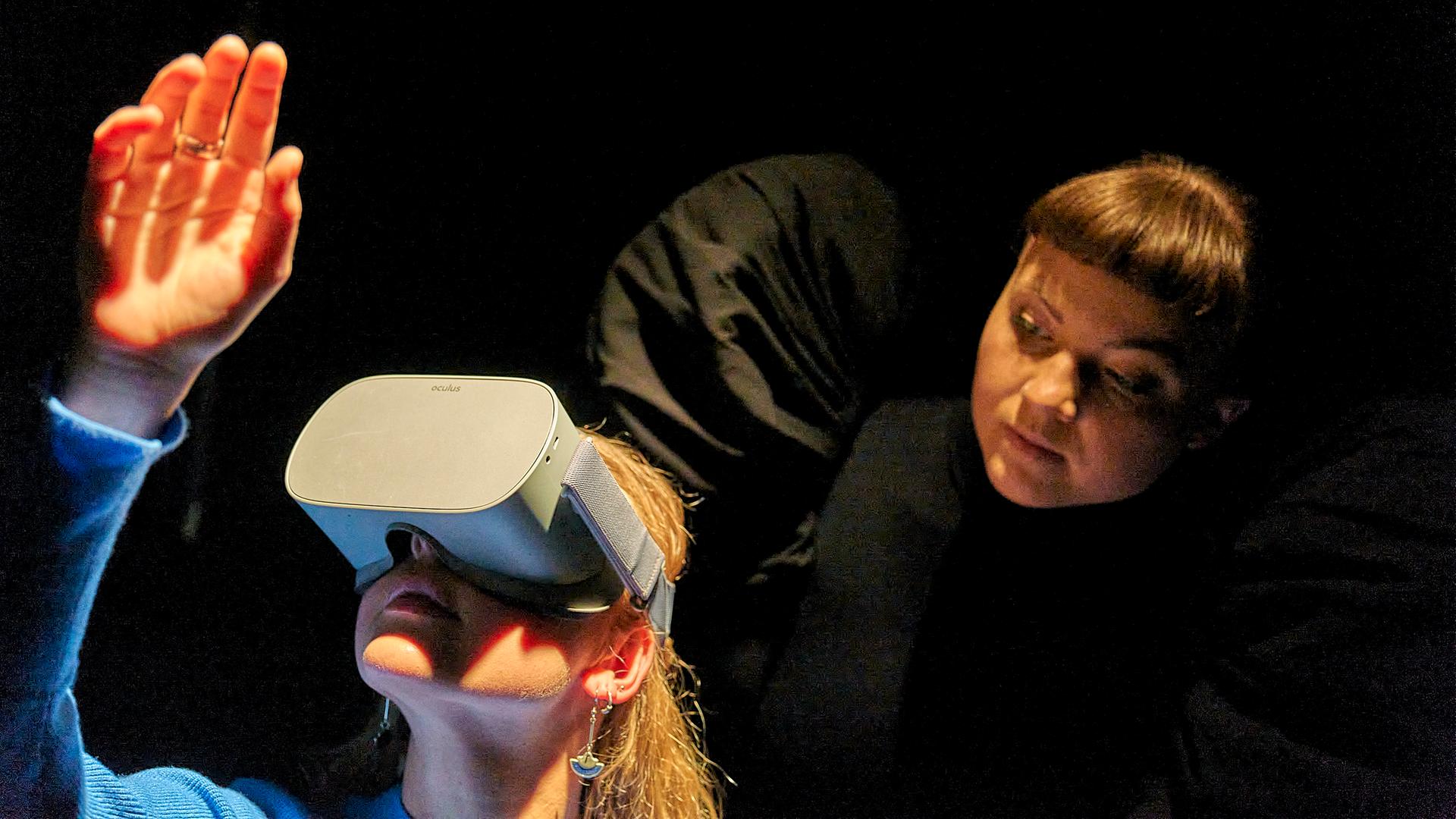 Eine Zuschauerin von "Berlau" im BE trägt eine VR-Brille. Hinter ihr eine Schauspielerin mit schwarzen Engelsflügeln. Eine Zuschauerin von "Berlau" im BE trägt eine VR-Brille. Hinter ihr eine Schauspielerin mit schwarzen Engelsflügeln.