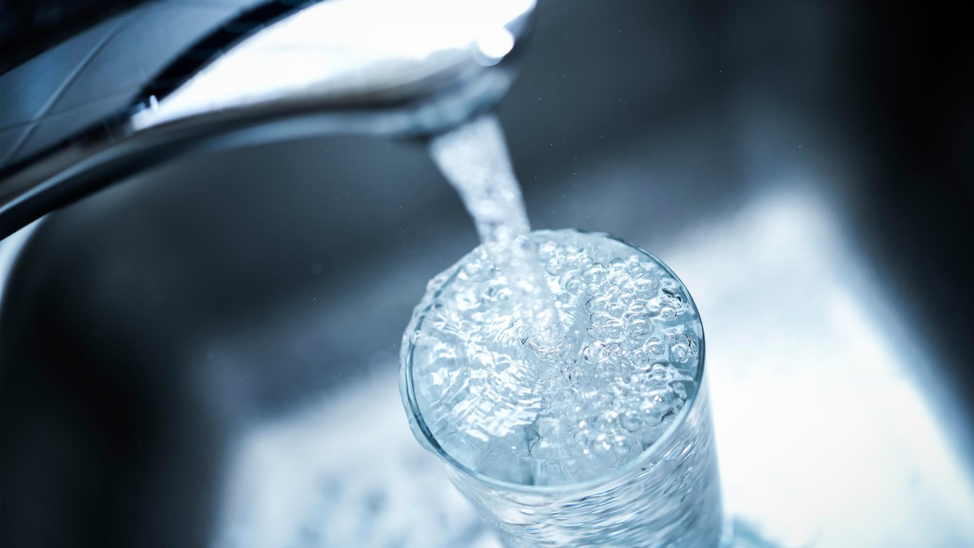 Wasser läuft von einem Wasserhahn in ein Glas.
