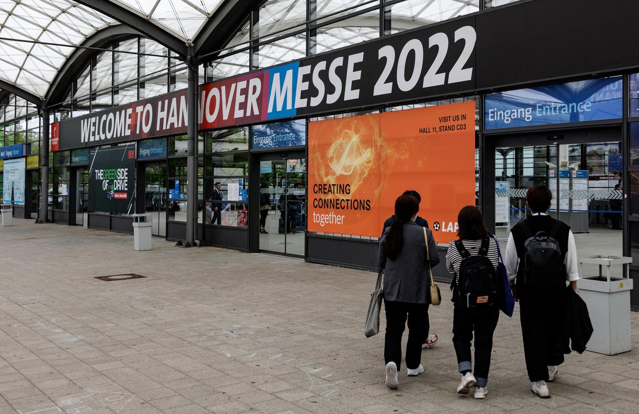 Drei Personen betreten einen Eingang der Messehalle Hannover.