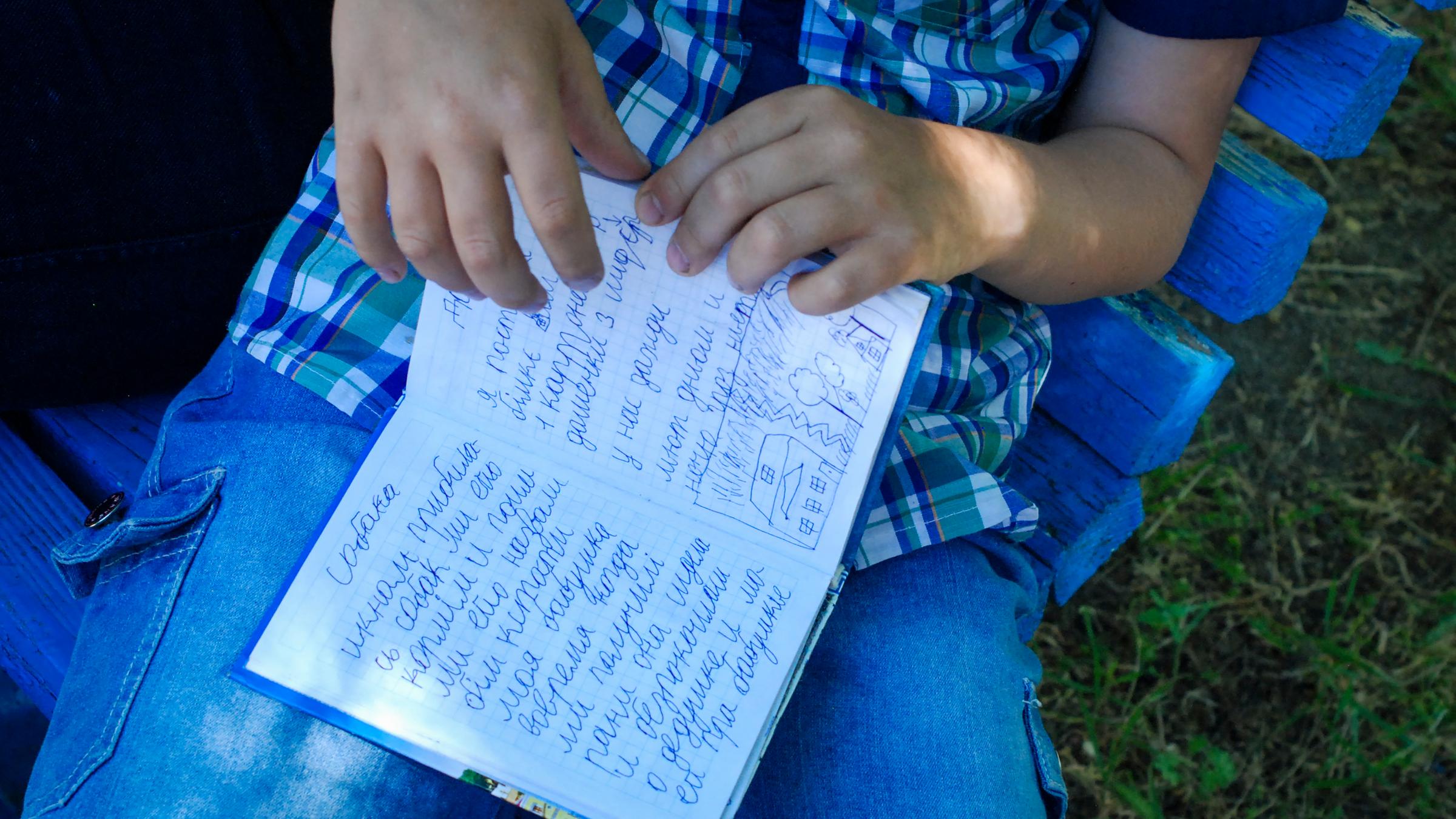 Der 8-Jährige Egor hält ein kleines blaues Buch in seiner Hand. Er hat in Mariupol Tagebuch geführt, als die Stadt blutig umkämpft war. Auf der aufgeschlagenen Seite steht neben einer kleinen Zeichnung: "Ich habe gut geschlafen, habe gelächelt und 25 Seiten gelesen. Ausserdem ist mein Grossvater gestorben am 26.April". Zaporizhzhia, 3.Juni 2022.