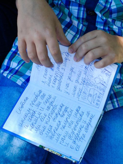 Der achtjährige Egor hält ein kleines blaues Buch in seiner Hand. Er schrieb in Mariupol Tagebuch, als um die Stadt blutig gekämpft wurde. Auf der aufgeschlagenen Seite steht neben einer kleinen Kinderzeichnung: "Ich habe gut geschlafen, habe gelächelt und 25 Seiten gelesen. Außerdem ist mein Großvater gestorben am 26.April. Saporischschja, 3. Juni 2022."