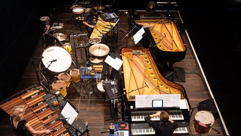Ein Blick von oben auf die spielenden Musiker auf der Bühne in den Korpus zweier Flügel und viel Schlagwerk
