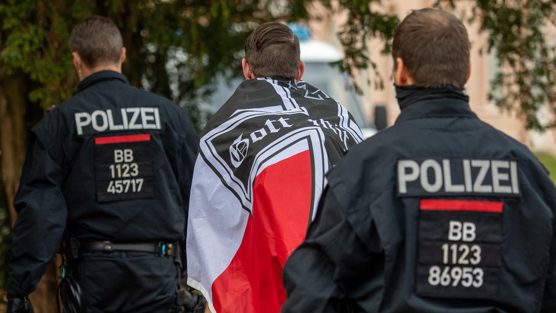 "Reichsbürger"-Demonstration im November 2020 in Potsdam: Ein Demonstrant mit einer schwarzrotweißen Flagge mit einem Eisernen Kreuz darauf wird von zwei Polizisten abgeführt. "Reichsbürger"-Demonstration im November 2020 in Potsdam: Ein Demonstrant mit einer schwarzrotweißen Flagge mit einem Eisernen Kreuz darauf wird von zwei Polizisten abgeführt.