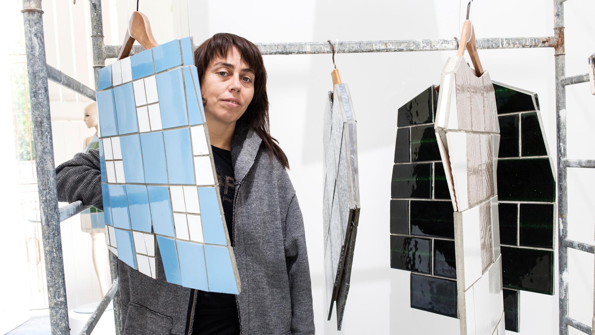 Die ukrainische Künstlerin Zhanna Kadyrova steht neben einem Kunstwerk von ihr: Kacheln, die an einem Kleiderbügel hängen. Die ukrainische Künstlerin Zhanna Kadyrova steht neben einem Kunstwerk von ihr: Kacheln, die an einem Kleiderbügel hängen.