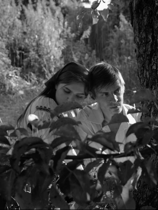 Schwarzweißaufnahme von einem jungen Mann und einer jungen Frau, die im Gebüsch sitzen