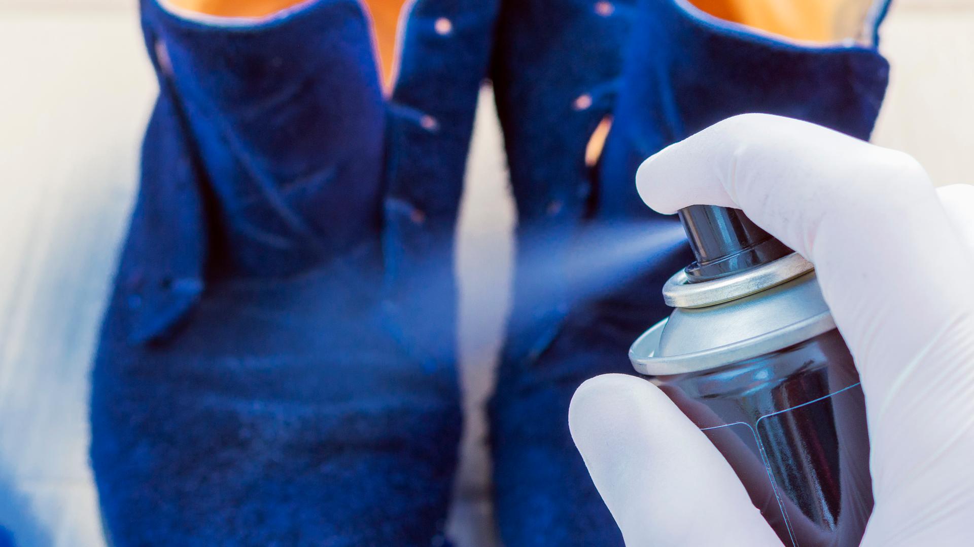 Eine Person sprüht, Gumminhandschuhe tragend, blaue Wildlederschuhe mit Imprägnierspray ein. Eine Person sprüht, Gumminhandschuhe tragend, blaue Wildlederschuhe mit Imprägnierspray ein.