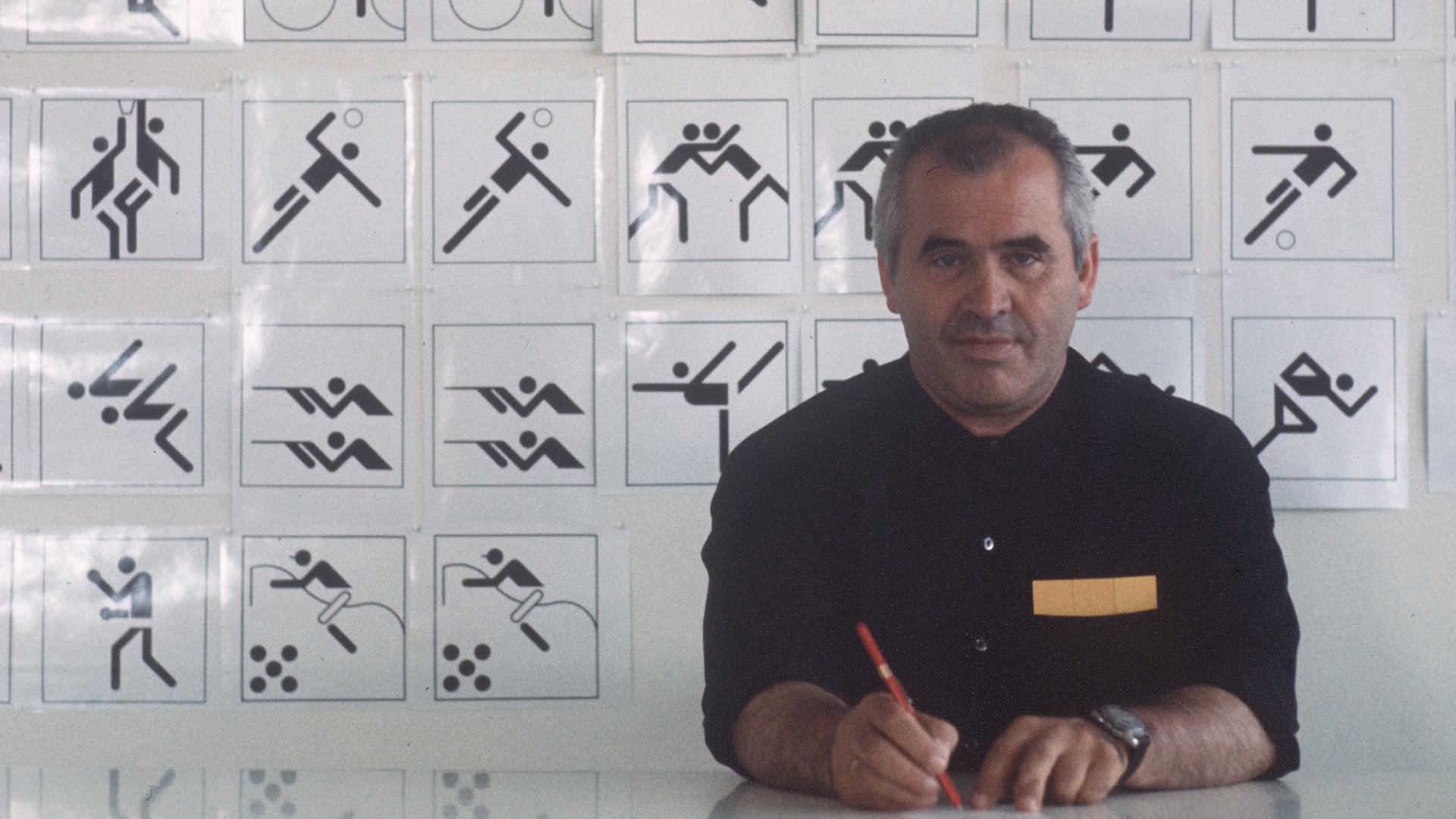 Der Grafiker, Designer, Architekt, Otl Aicher (1922-1991) sitzt 1970 an seinem Schreibtisch, im Hintergrund eine Tafel mit Piktogrammen, Symbolen, Zeichen, die er für die Sportarten der Olympischen Sommerspiele 1972 in München entworfen hat.