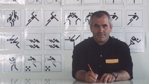 Der Grafiker, Designer, Architekt, Otl Aicher (1922-1991) sitzt 1970 an seinem Schreibtisch, im Hintergrund eine Tafel mit Piktogrammen, Symbolen, Zeichen, die er für die Sportarten der Olympischen Sommerspiele 1972 in München entworfen hat