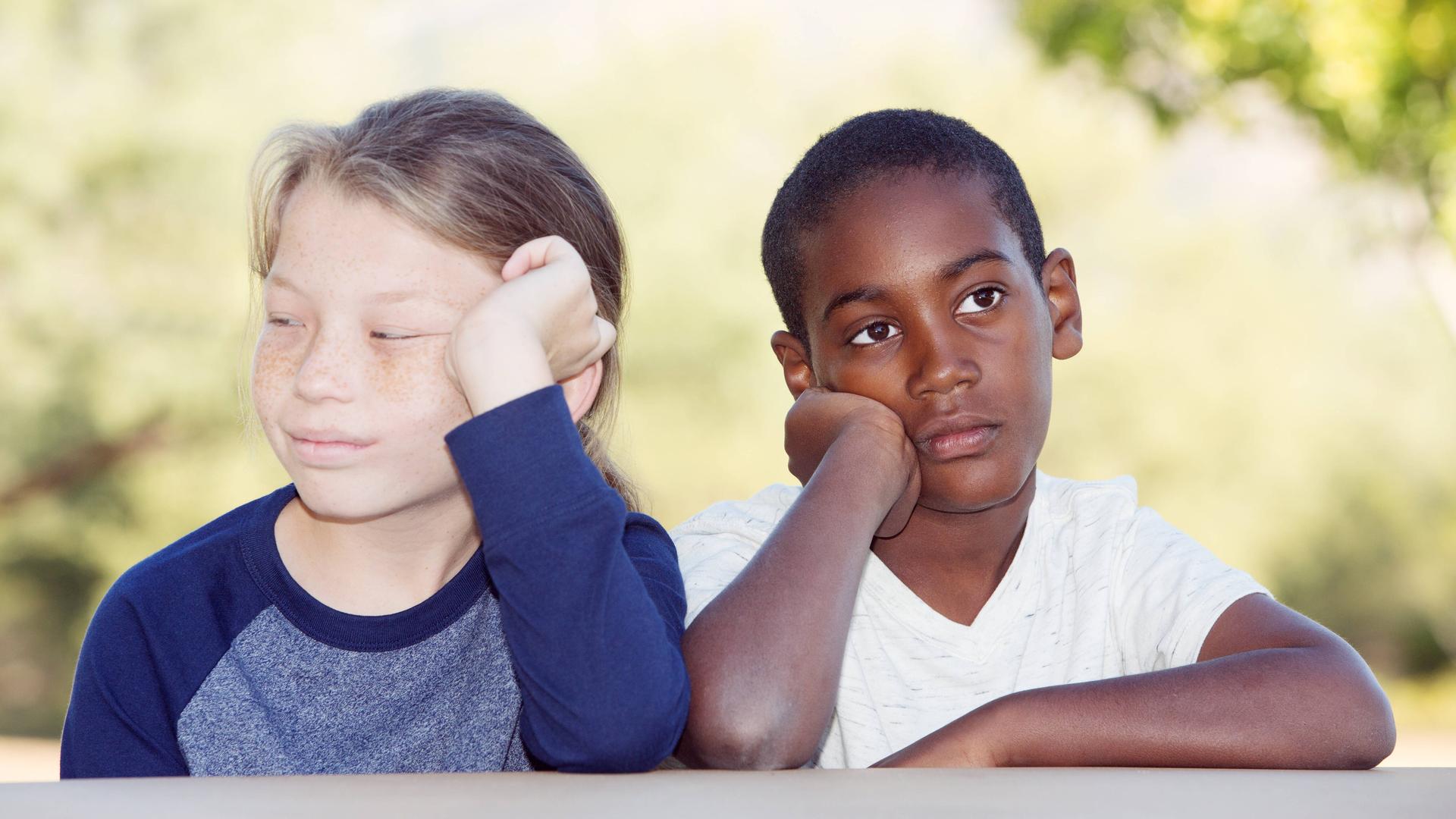 Zwei Kinder sitzen nebeneinander, beide mit gelangweiltem Gesichtsausdruck und die Köpfe auf die Hände gestützt. Zwei Kinder sitzen nebeneinander, beide mit gelangweiltem Gesichtsausdruck und die Köpfe auf die Hände gestützt.
