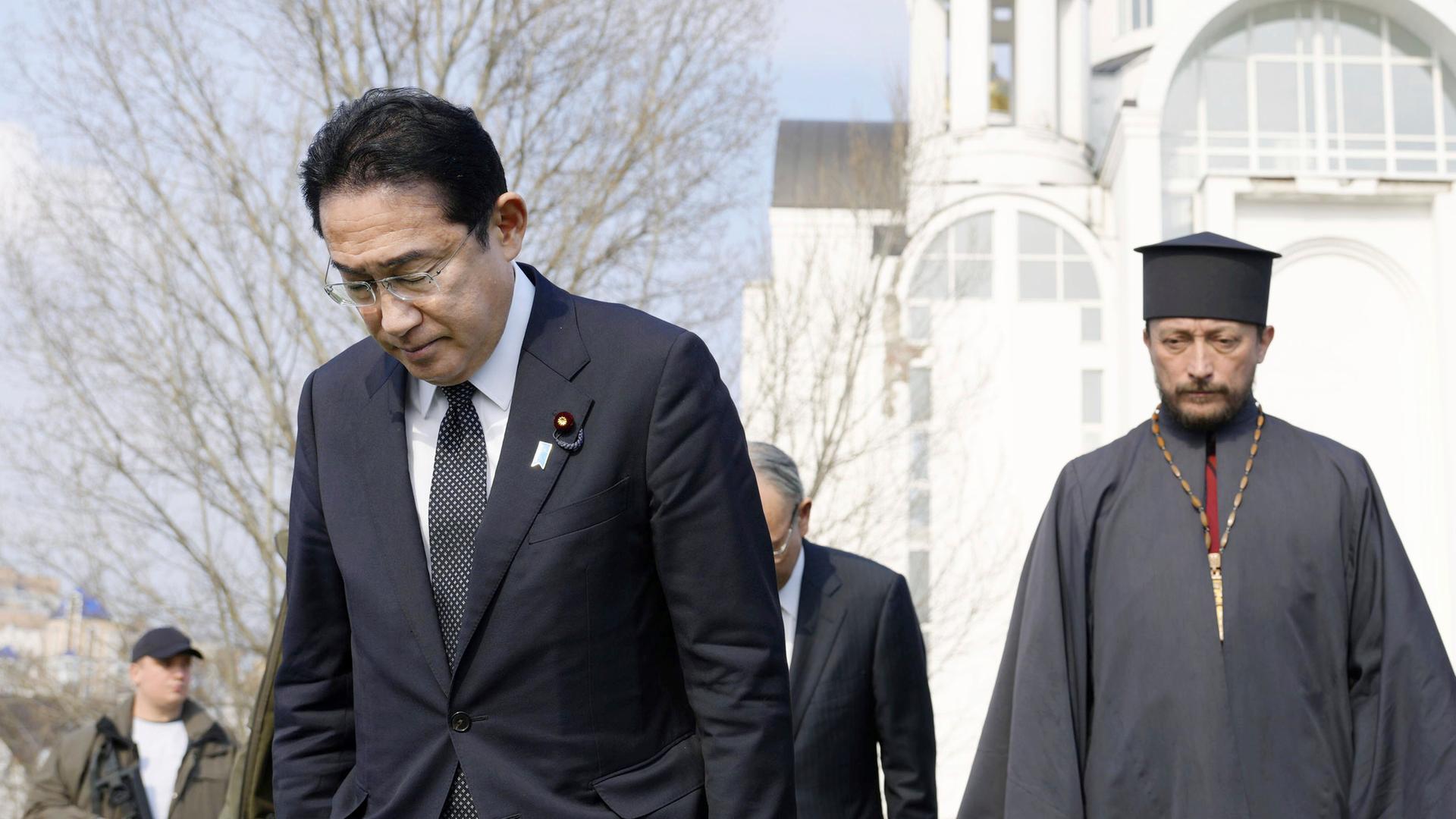 Kishida steht vor einer Kirche, neben ihm steht einer Priester. Kishida senkt den Kopf. Kishida steht vor einer Kirche, neben ihm steht einer Priester. Kishida senkt den Kopf.