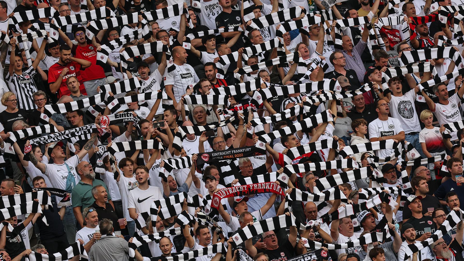 Fußball-Fans von Eintracht Frankfurt in einem Stadion. Sie halten gestreifte Fan-Schals in die Höhe. Fußball-Fans von Eintracht Frankfurt in einem Stadion. Sie halten gestreifte Fan-Schals in die Höhe.