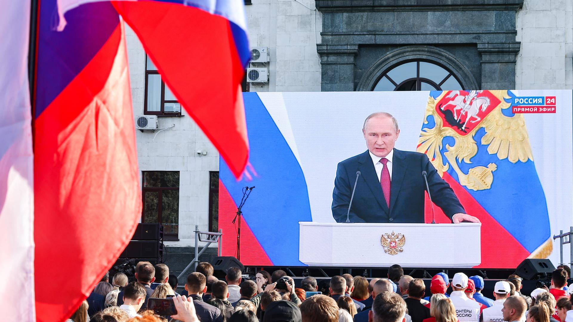 Auf einer großen Leinwand wird die Rede des russischen Präsidenten Wladimir Putin übertragen. Seine Anhänger stehen davor.