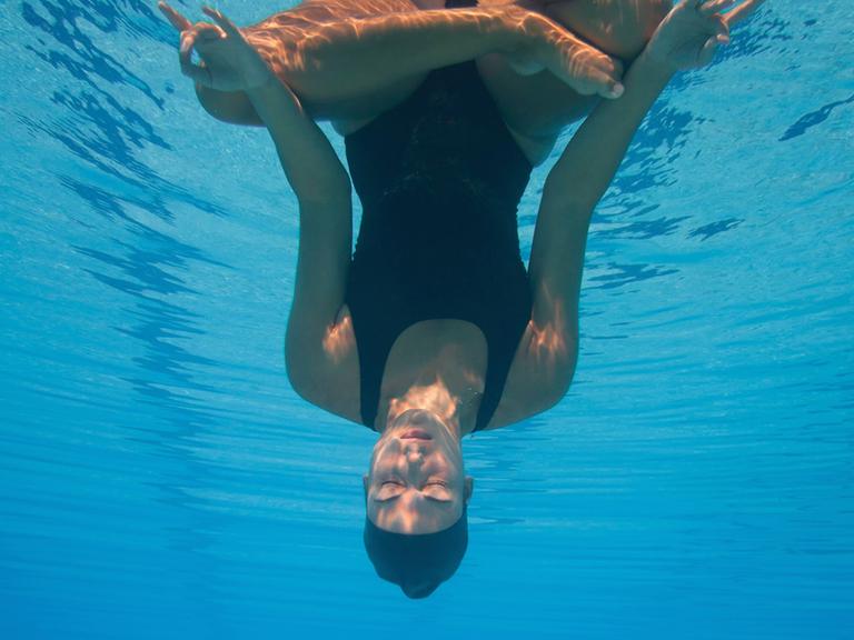 Eine Frau kopfüber unter Wasser in Meditationshaltung.